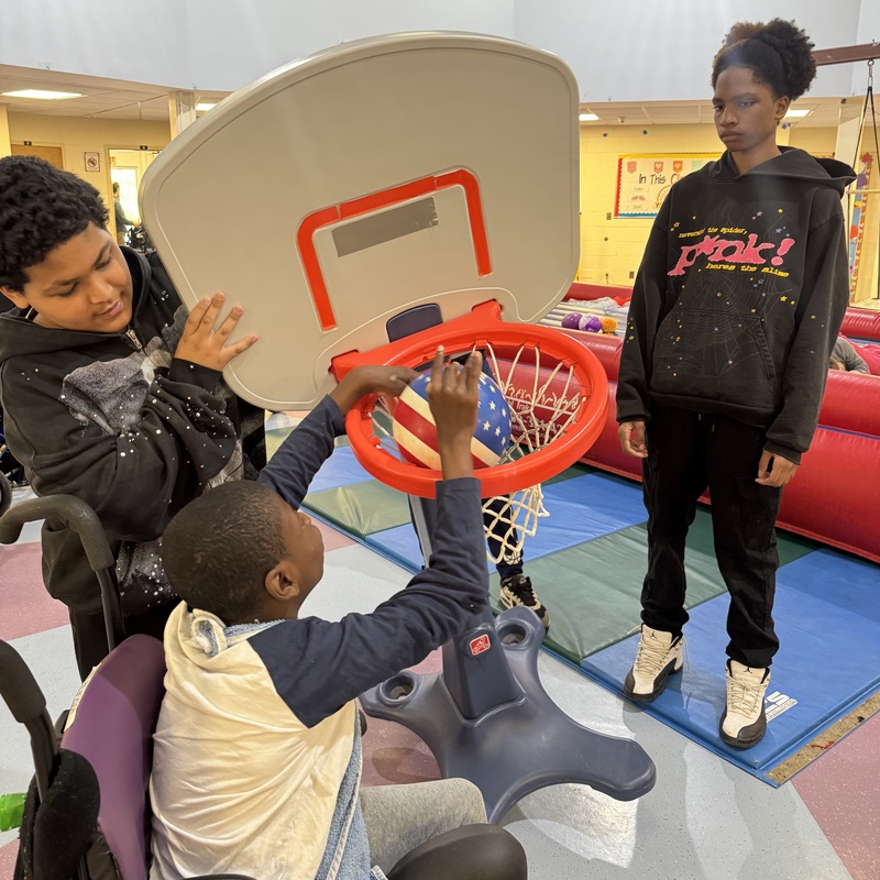 student holds basketball net for student to shoot basketball