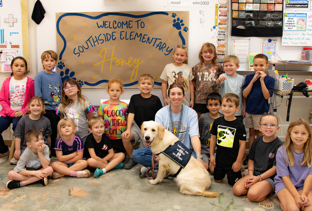 students and teacher gathered around white lab dog