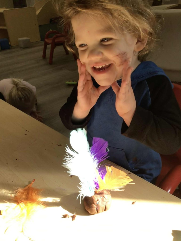 child putting feathers in playdoh