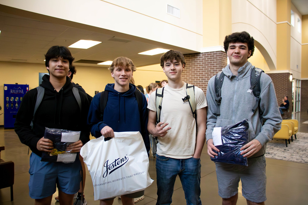 Four senior boys holding bags and cap and gown