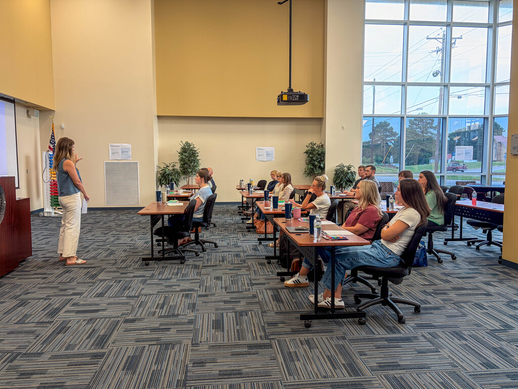 teachers sitting at tables listening to a woman speak