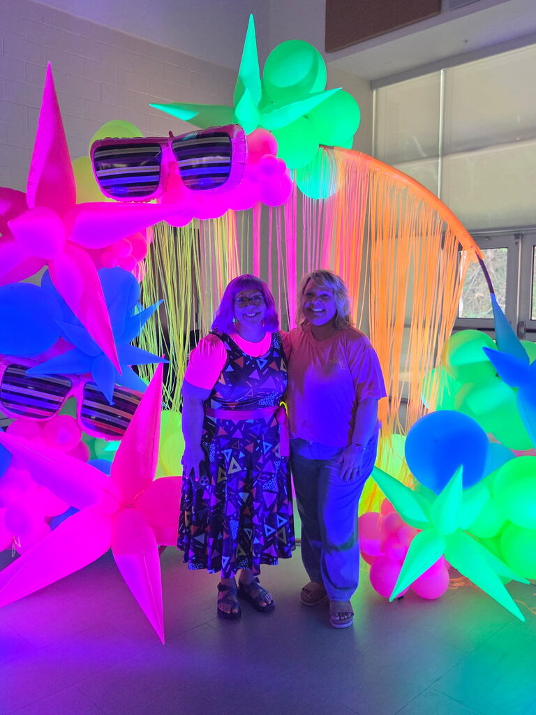 two women in bright neon in front of glow in the dark balloons 