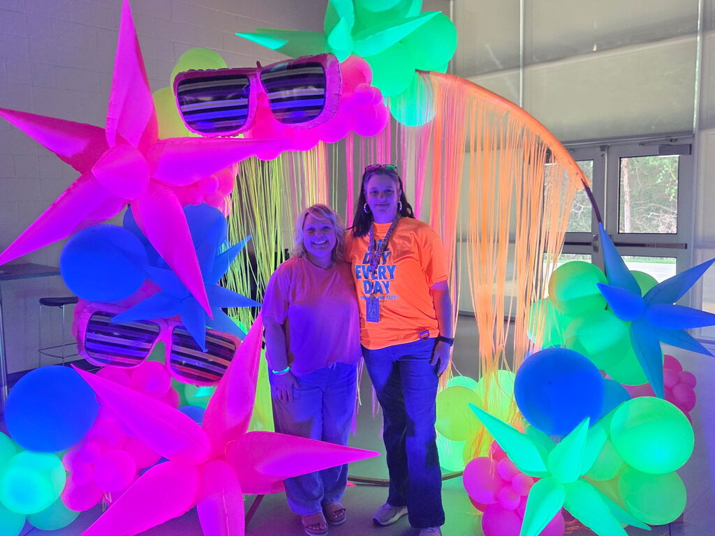 two women in bright neon in front of glow in the dark balloons 