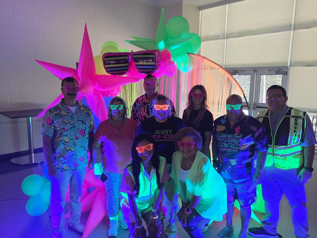 group of men and women in bright neon in front of glow in the dark balloons 