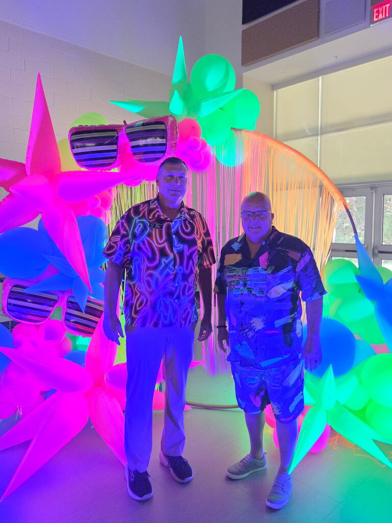 two men in bright neon in front of glow in the dark balloons 