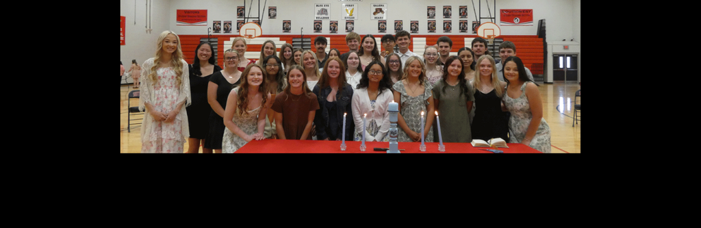 This photo captures the full group of 2026 NHS members at Southwest High School. The lit candles on the red-draped table in the foreground serve as a central symbol of the ceremony's tradition and the students' academic commitment.