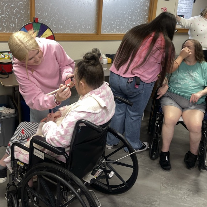 young women applying makeup to elderly women 