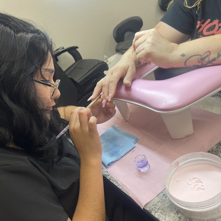 adult cosmetology student performing acrylic nail service