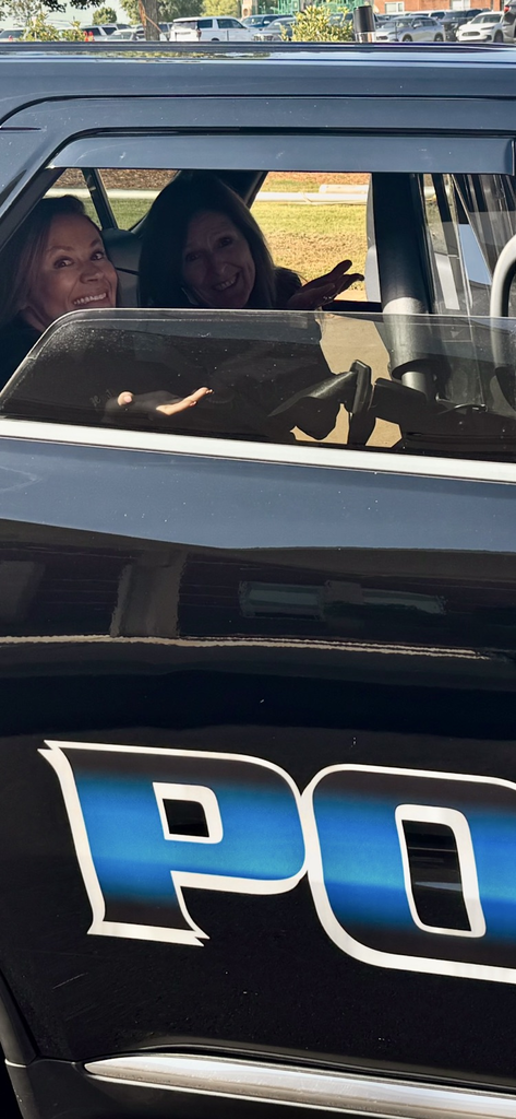 two women smiling and waving from the backseat of a District resource officer’s car