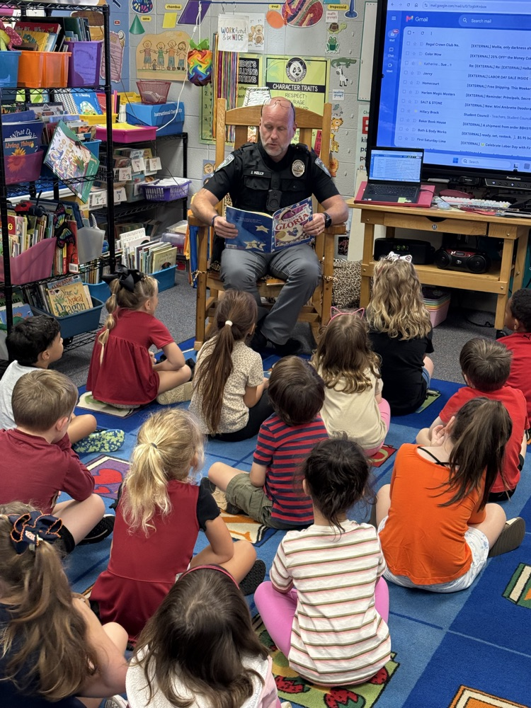 police officer sitting in chair reading to students sitting on the floor 