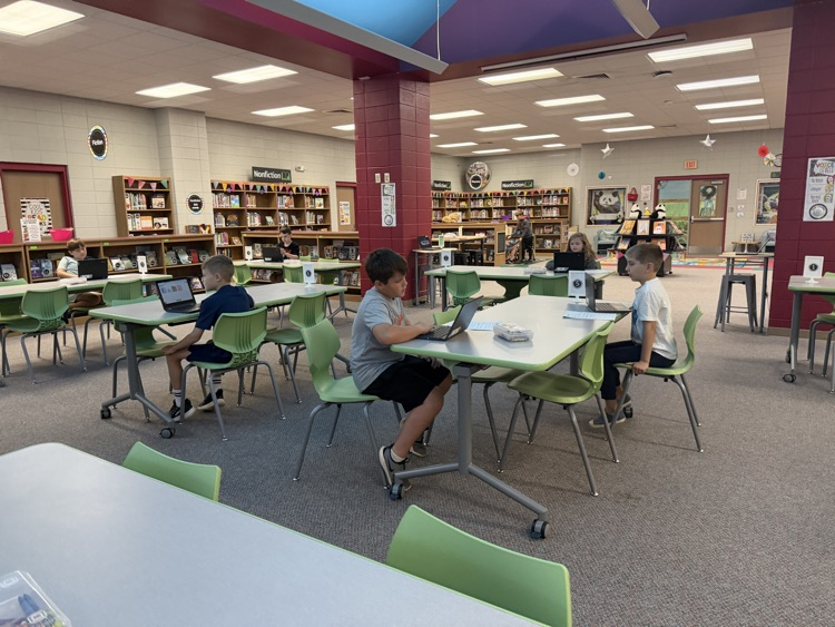 students in the library recording podcasts on laptops