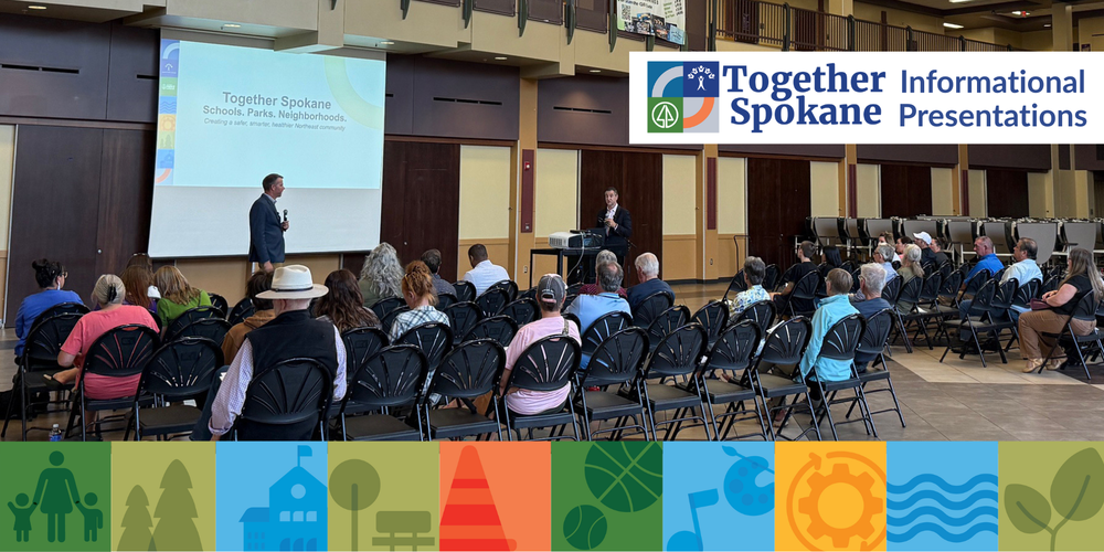 Two men speak to a large group of community members seated in folding chairs in a high school cafeteria with a presentation titled Together Spokane behind them.