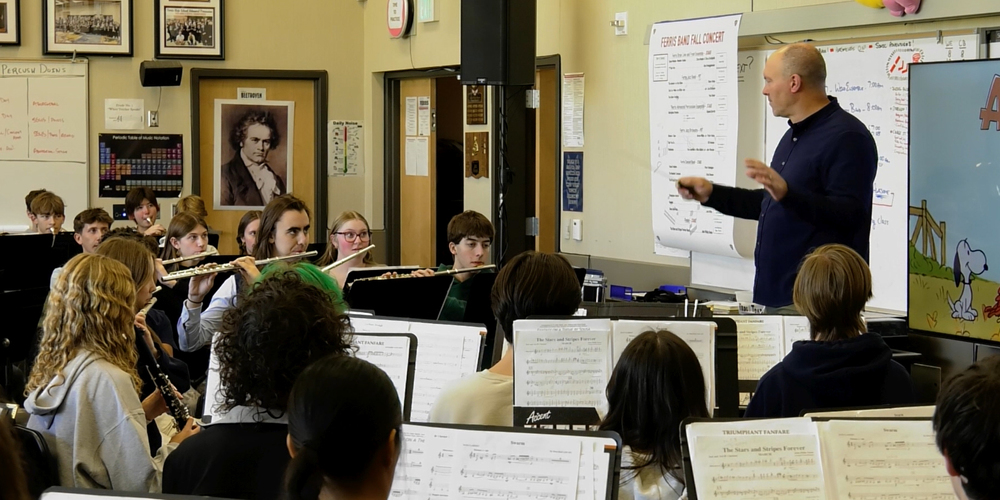 A band teacher directors high school students in a classroom.