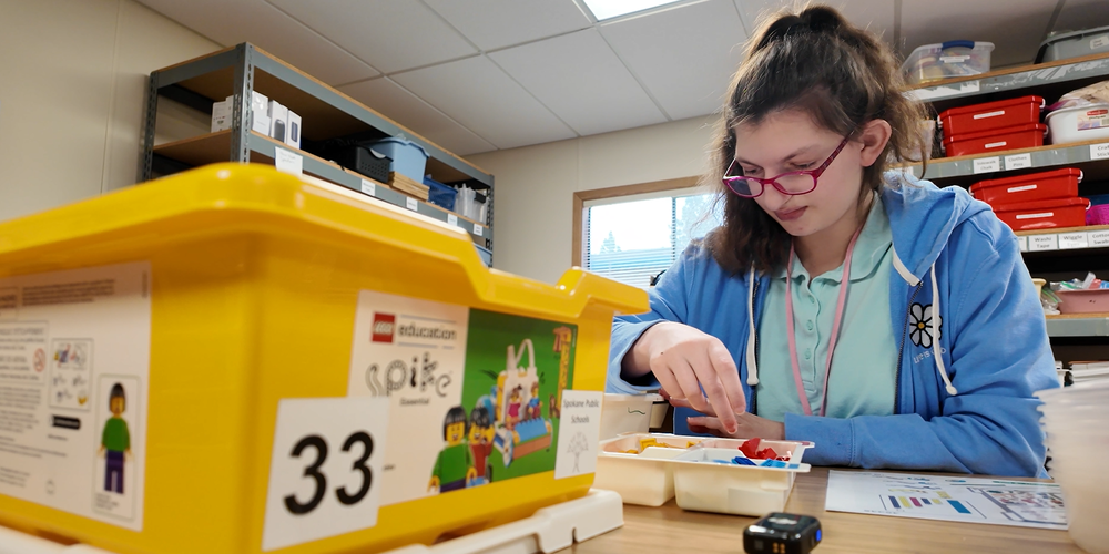 A student sorts LEGO bricks to collect in a yellow tub.