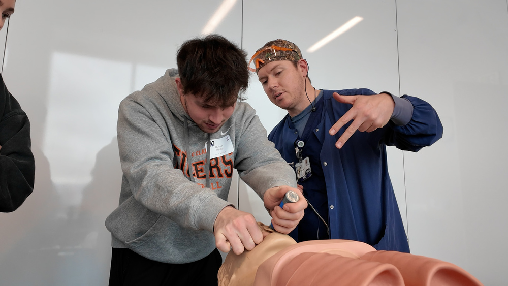 A medical profession helps a student learn intubation on a medica mannequin.