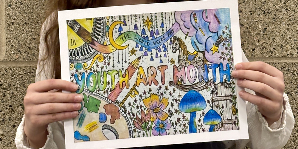 A middle school holds a colorful drawing incorporating the text “The World Needs Art” and “Youth Art Month” into a design with painting materials, clouds, flowers, mushrooms, a rocking horse and a rustic wooden door with a skeleton key.