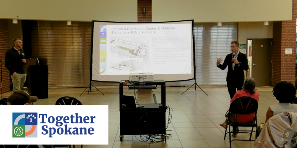 Garrett Jones and Adam Swinyard present information to an audience of people in a school auditorium.