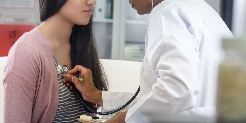A medical professional uses a stethoscope to listen to a young woman's heart.