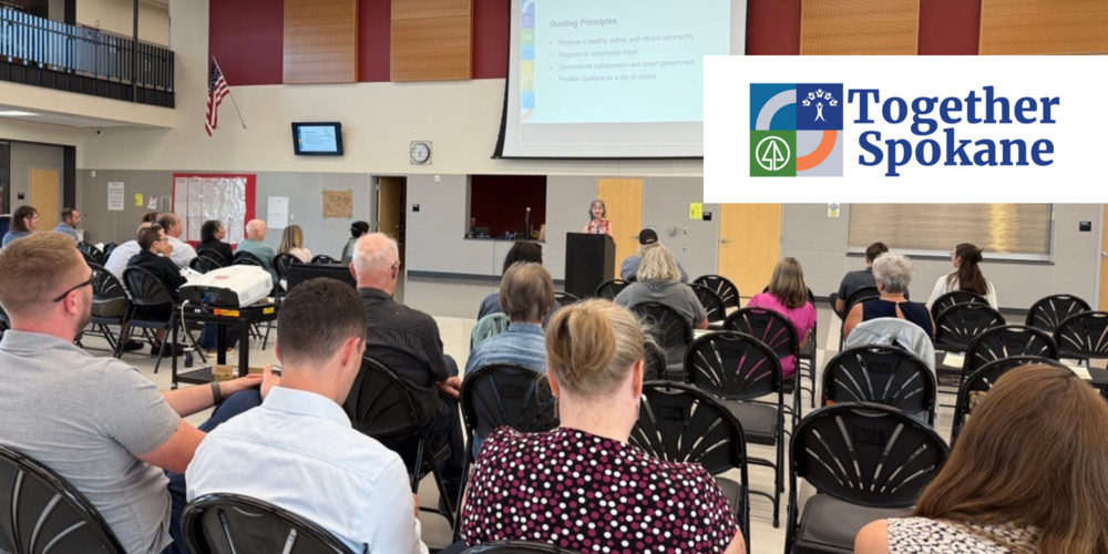 A woman speaks at a lectern to an audience of people with the logo for Together Spokane.