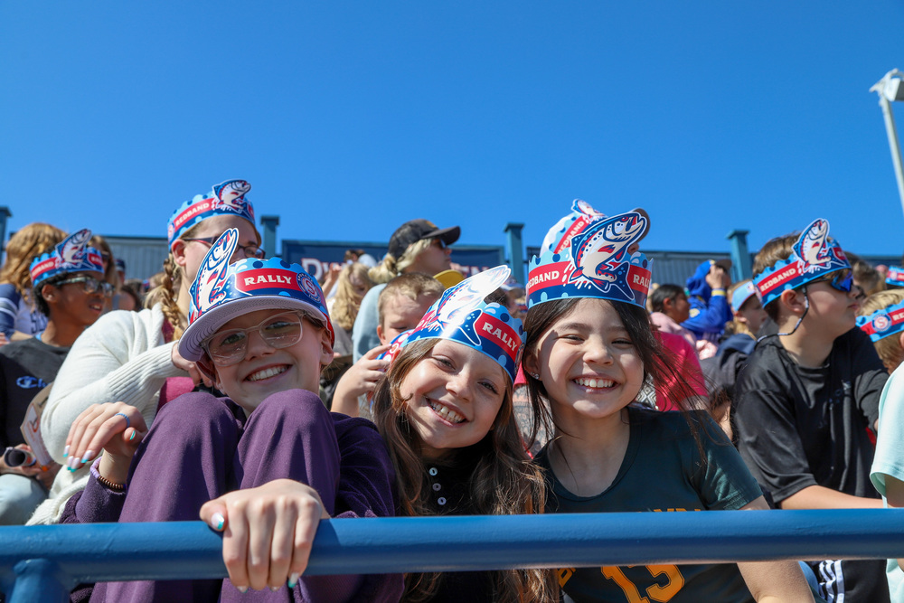Elementary school students smile in the stands of a baseball stadium during a game.