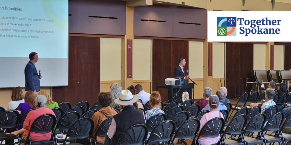 Two men present information to people seated in folding chairs with the logo for Together Spokane included.