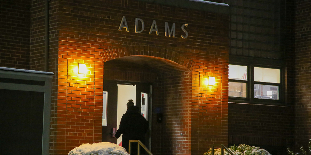 People enter Adams Elementary School, illuminated by light on a snowy, winter night.