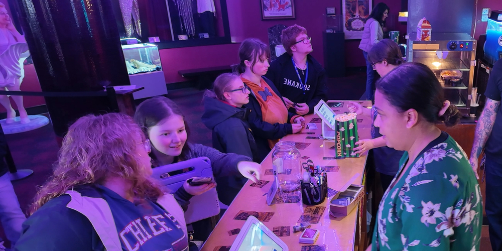 Students and staff purchase concessions at a movie theater counter.