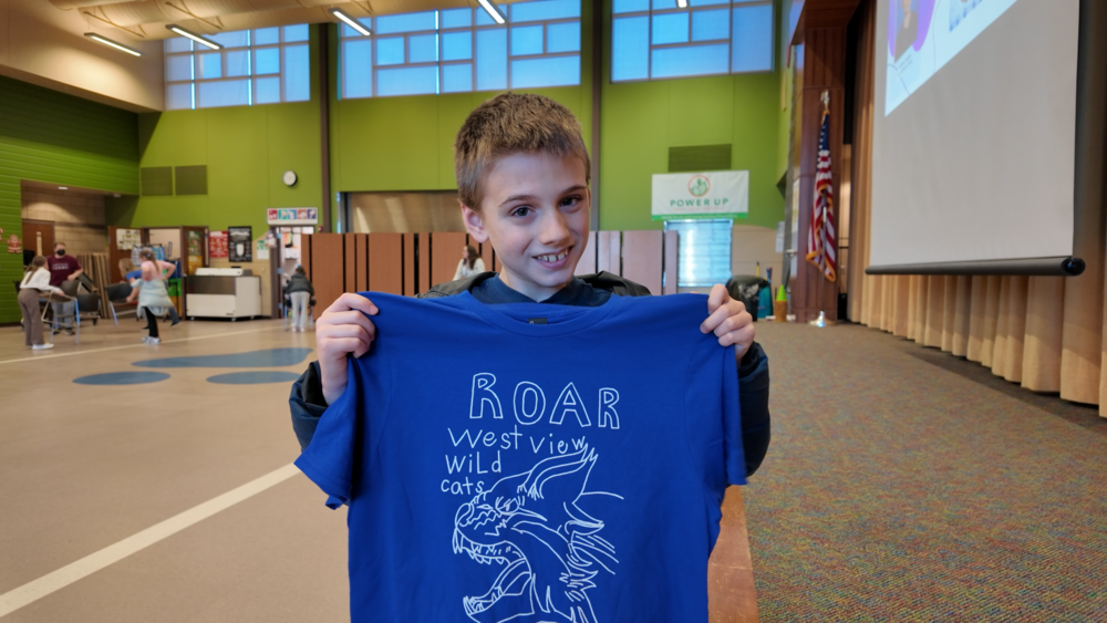 Westview 4th grader Hudson holds a blue t-shirt with his Westview Wildcast design.