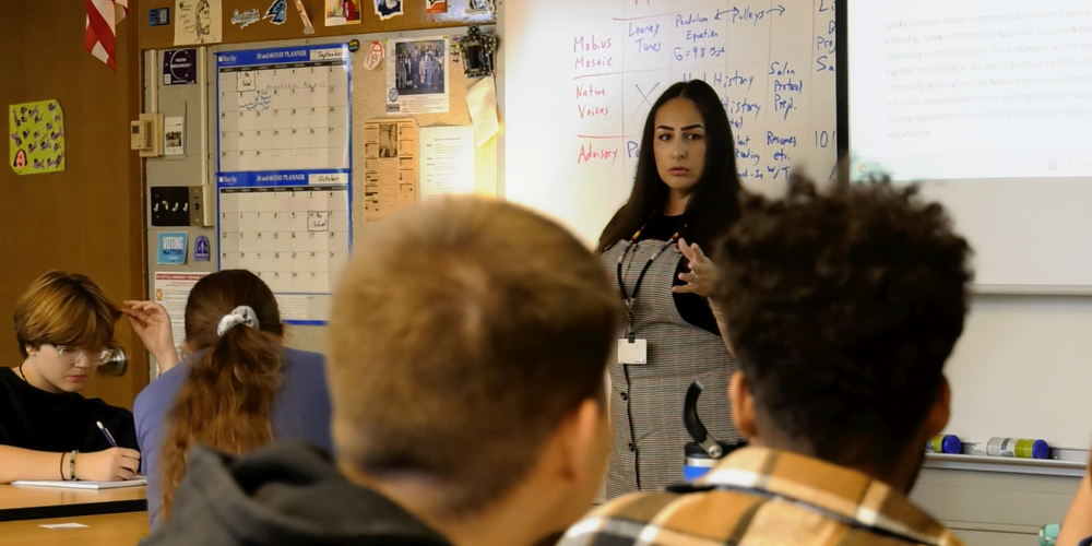 A guest speaker stands in front of a classroom of high school students.