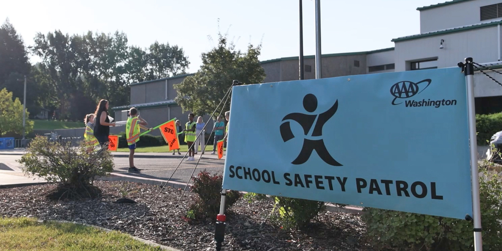 A AAA Washington School Safety Patrol sign and crossing guards outside an elementary school.