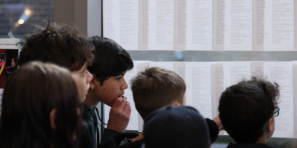 Middle school students look for their name and Falcon Time assignment on papers posted on windows.
