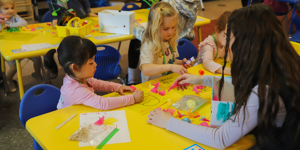 A teacher helps preschool students with markers and crafts.