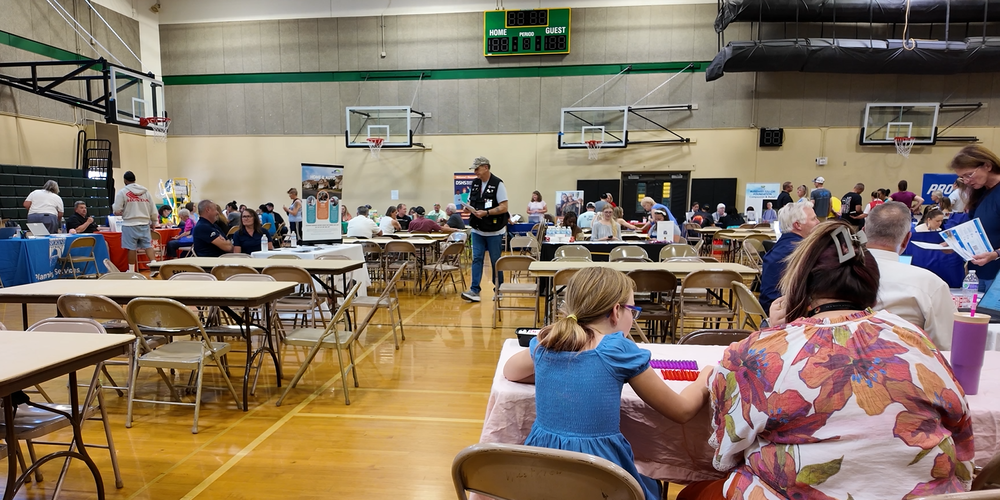 People gathered at folding tables and chairs in a high school gym for wildfire recovery support.