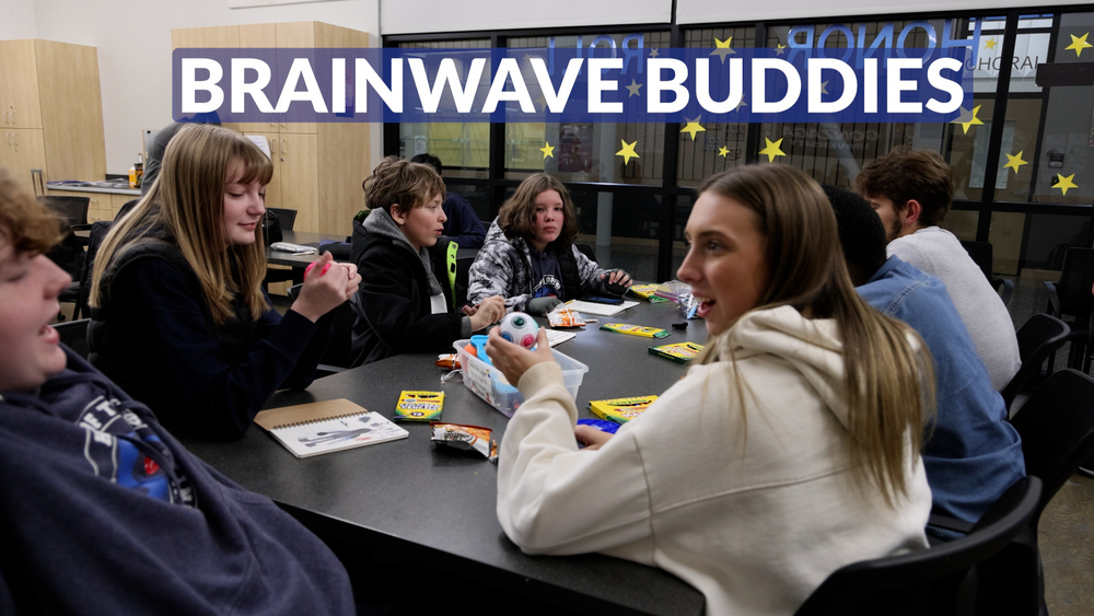 Middle school and college students sit around a table with art supplies in a classroom. Text reads Brainwave Buddies.