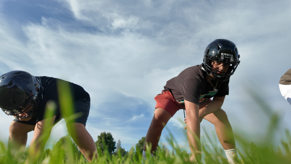 Middle school students practice football on a grassy field.