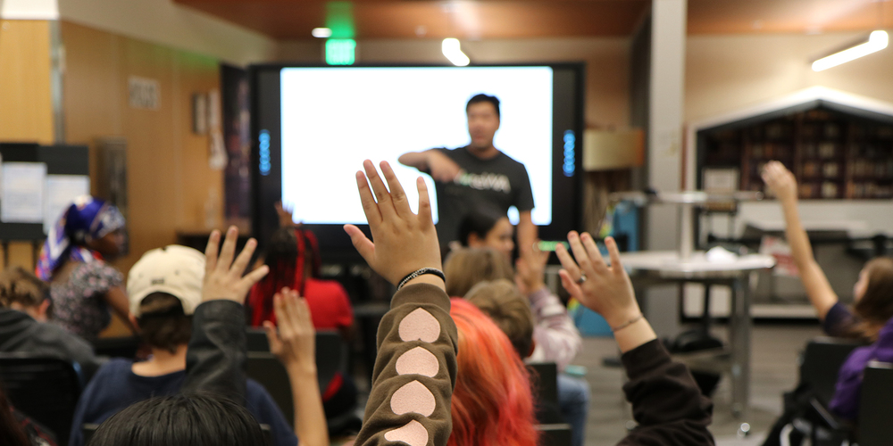 Middle school students raise their hands during a presentation about elections.