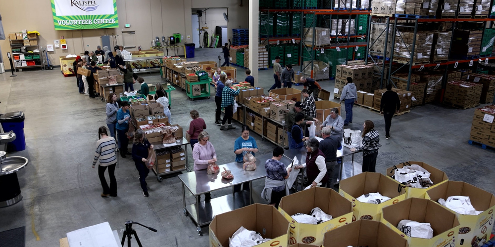 Volunteers in a warehouse pack bags with food.