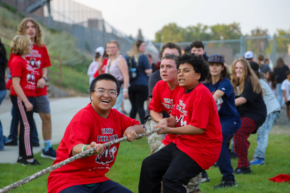 North Central High School students wearing red shirts smile as they participate in a tug of war competition.