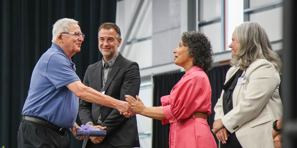 Retirees and award winners are recognized on stage in a large venue.