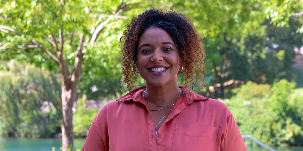 Natalie Marhsall smiles outside a park with a river.