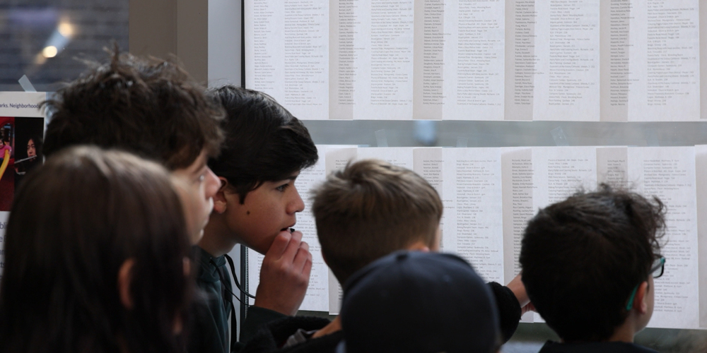 Middle school students look for their name and Falcon Time assignment on papers posted on windows.