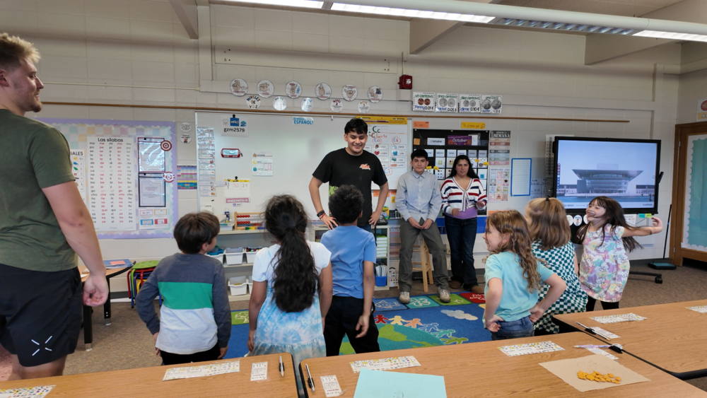 Rogers High School students stand in front of TDLA students in a classroom.
