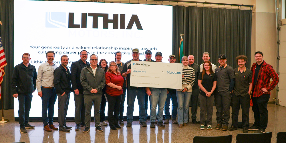 Representatives from Lithia Motors present an oversized check for $50,000 to students and staff on a stage at NEWTech Prep.