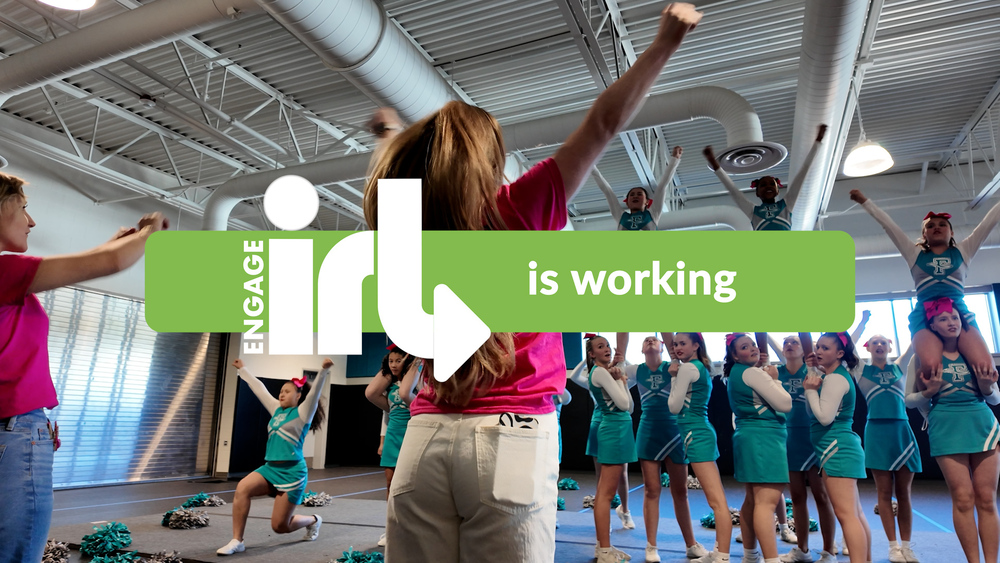 A coach leads a cheer squad in a practice with text reading "Engage IRL is working."