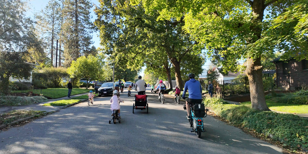 Adults and children riding bicycles through a neighborhood.
