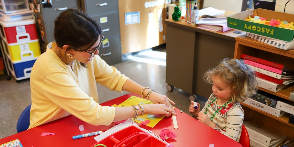 A high school student helps a preschool student with a craft.