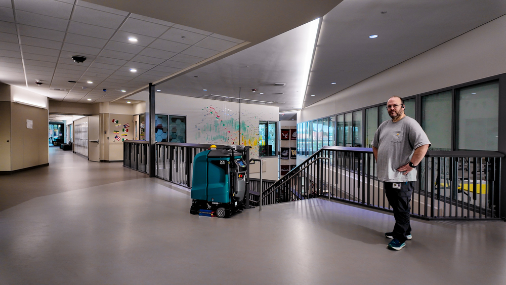Man stands with cleaning robot near staircase in a school.