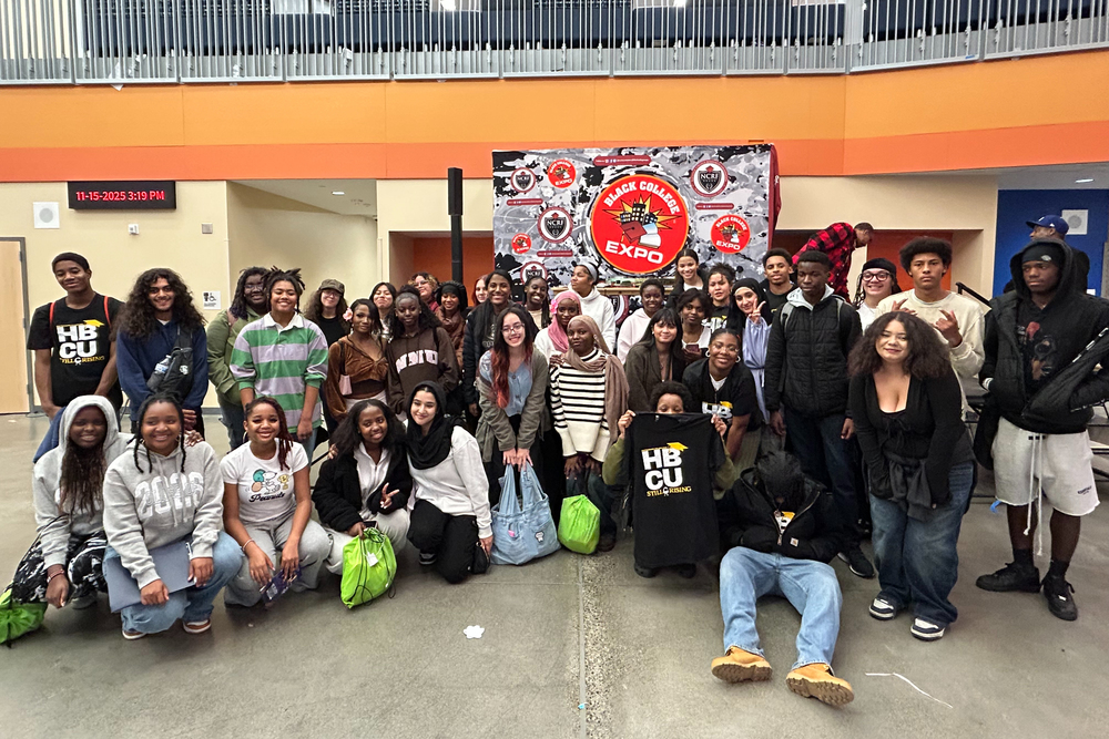 A large group of diverse students smile next to a sign for Black College Expo.