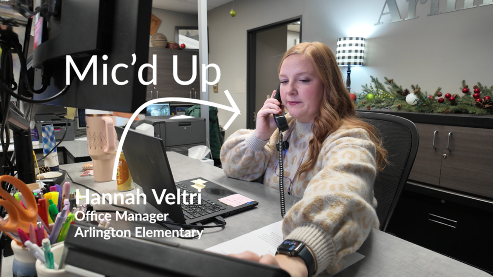 Arlington Elementary School Office Manager Hannah Veltri answers the phone at her desk in a Mic'd Up video.
