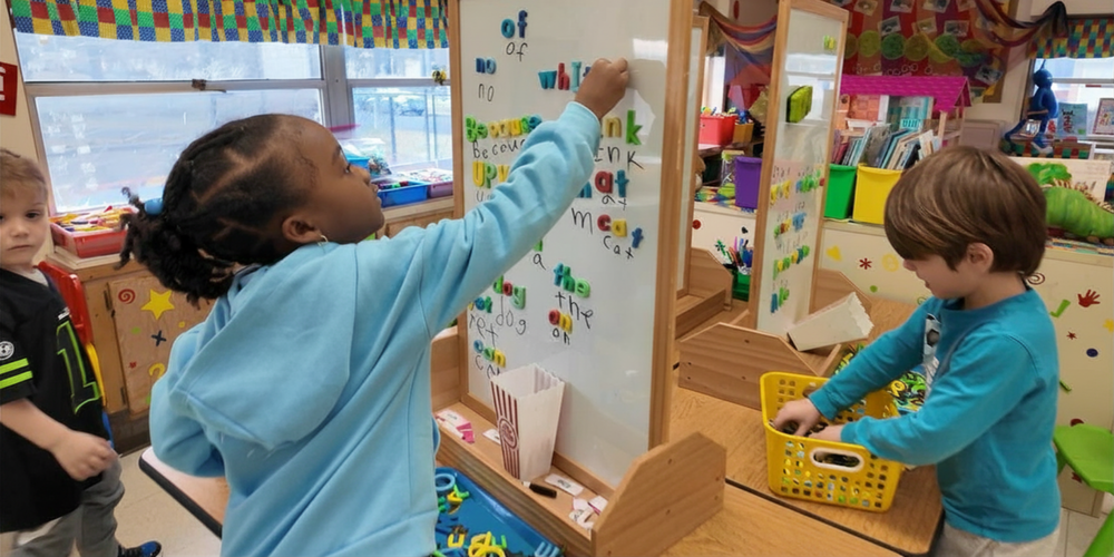 Kindergarten students place magnetic letters on a white board in a classroom.